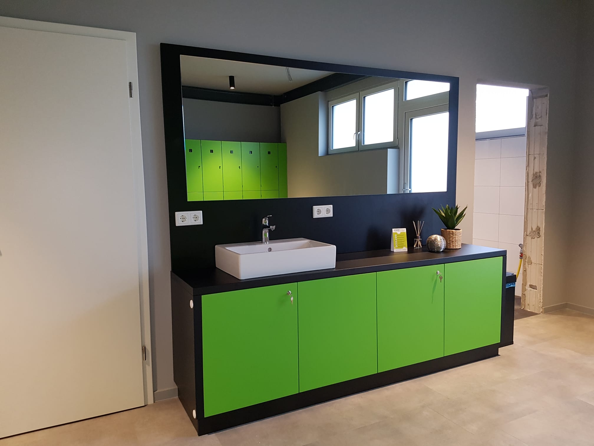 Moderne Badezimmermöbel in leuchtendem Grün mit einem weißen Waschbecken und großem Spiegel.