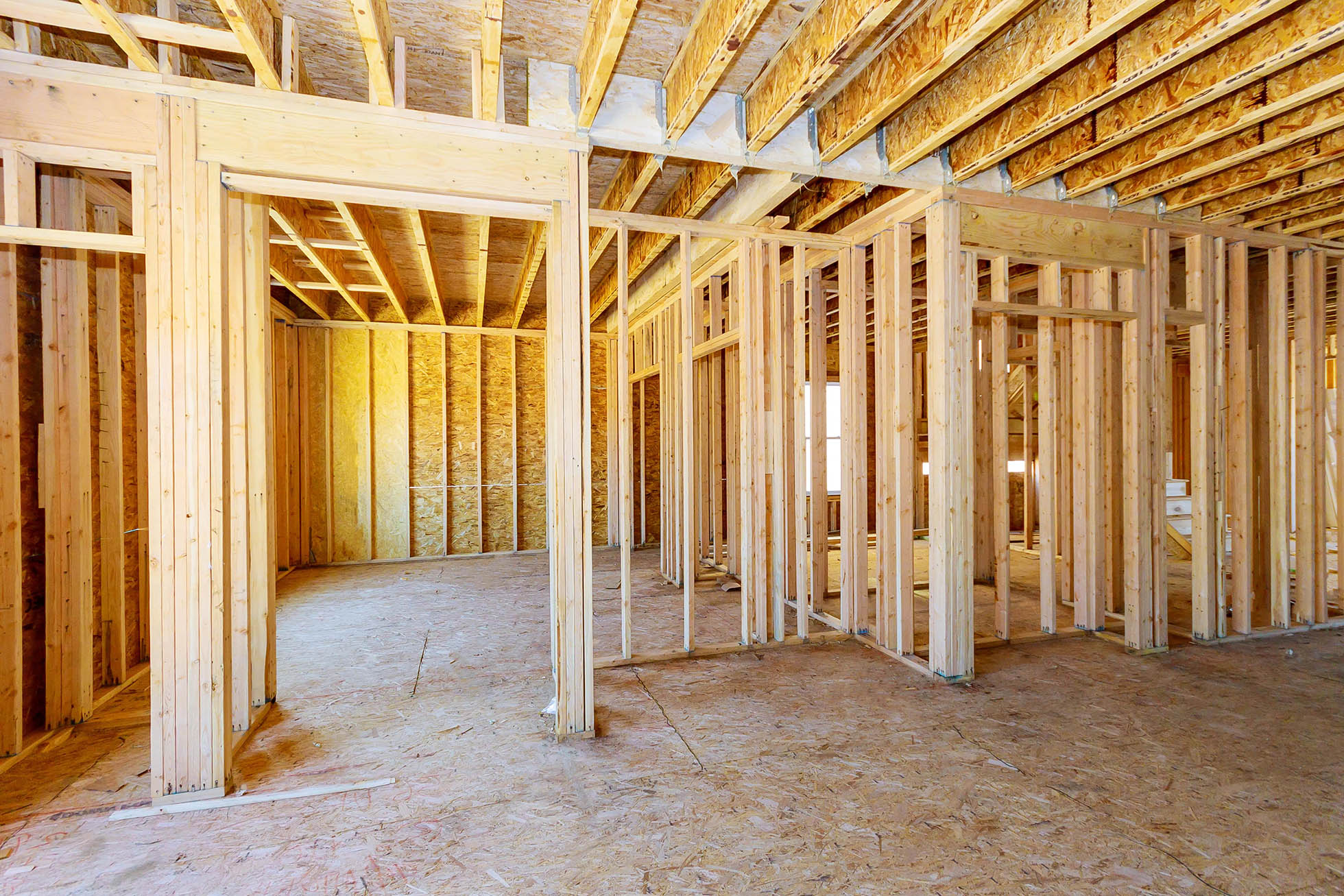Holzständerwerk und offene Innenwände in einem Neubau mit sichtbaren Deckenbalken, OSB-Platten und mehreren Raumteilungen im Rohbau.